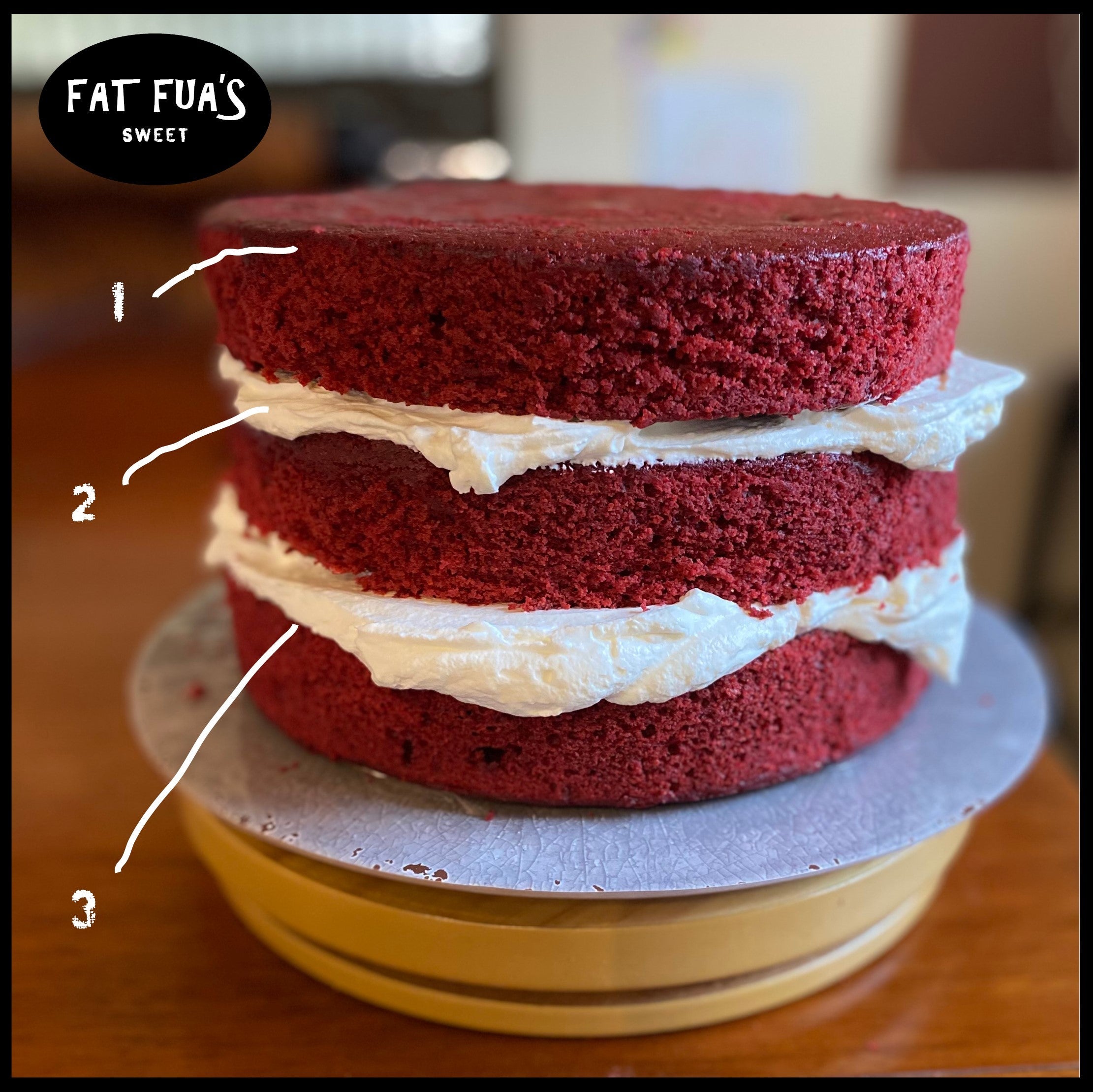 Photo of 3 layers of moist red velvet cake sandwiched in between whipped cream cheese frosting on a wooden spinning trivet  